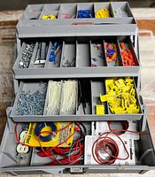 Opened organizer case displaying multiple compartments filled with electrical connectors, zip ties, screws, wires, and tools
