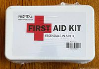 Front view of white plastic ProHeal first aid kit box showing label 'FIRST AID KIT ESSENTIALS IN A BOX'
