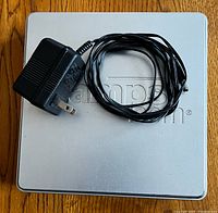 Top view of silver square postal scale with power adapter and cord placed on top.