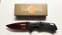Photo showing the folding pocket knife with the blade open facing left next to the Wild Boar branded box.