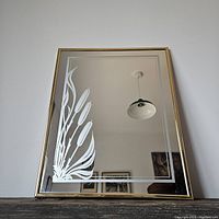 Frontal view of the rectangular mirror showcasing the etched cattails design on the left lower corner, with a gold metal frame and reflective surface.