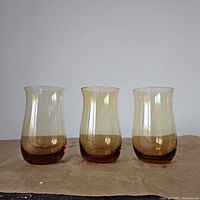 Front view of three vintage amber tulip glasses arranged side by side with visible translucent amber coloration
