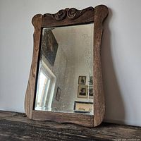 Full view of antique beveled mirror in wooden frame with carved top detail.