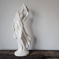 Full view of white ceramic figure showing elegant woman in flowing gown with flowers in hand.