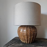 Full view of vintage ceramic lamp with woven basket style base and beige fabric shade on wooden surface.