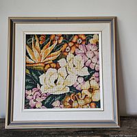 Full frontal view of the framed large floral needlepoint artwork showing colorful stitched flowers in shades of yellow, pink, orange, and green in a square frame with linen mat.