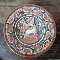 Top-down view of the circular ceramic plate showing detailed handpainted deer and surrounding floral patterns in earth tones.