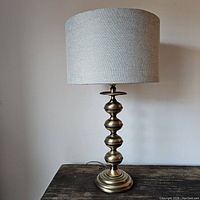 Full view of the vintage brass table lamp with fabric shade on a wooden surface against a blank wall.