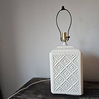 Front angle view of white ceramic lamp displaying rectangular shape, geometric pattern, and metal lamp socket