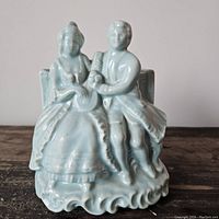 Front view showing romantic couple ceramic figurine attached to baby blue planter, highlighting details of clothing and faces.