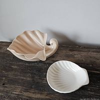 Photo showing both ceramic shell vessels side by side on a wooden surface against a plain wall.