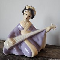 Full view of the vintage Geisha ceramic figurine sitting with a stringed instrument.
