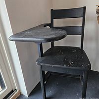 Side angle photo of the black wooden school chair with attached desk surface, showing wear on the seat and desk.