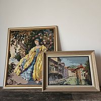 Two framed vintage needlepoints, one of a lady in a garden scene and one of Venice canal, both framed with glass.