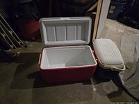 Open view of red Coleman cooler and beige Thermos cooler side by side on concrete floor