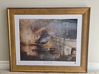 Framed print of the artwork showing the burning houses and bridge with detailed colors and gold wooden frame.