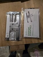 Two new small H-shaped BBQ burners in sealed plastic packages with informational inserts, laid flat on a wooden surface.