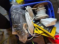 Overview of blue plastic bin filled with new recessed lighting units, coiled white wiring spools, black wiring, LED bulb packaging, and boxed electrical components.
