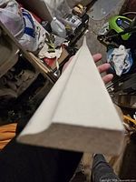 Close-up photo of white shoe molding piece held in hand showing profile and end grain for assessing shape and material