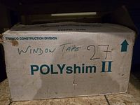 Cardboard box labeled 'POLYshim II' with handwritten 'WINDOW TAPE 27' text, showing box condition and contents storage.