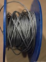 Close-up of the coiled 1/8 inch galvanized wire rope on a blue spool, showing the metallic braided construction.