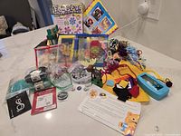 Wide view of assorted craft supplies including cross stitch kits, yarn, glass stones, puppets, frames and beads.