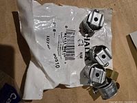 Four metal clamp connectors on top of a Halex branded bag