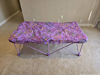 Side view of the Toys'R'Us Junior Anywhere Bed showing the folded metal legs and purple butterfly fabric mattress.