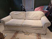 Front view of the white fabric sofa couch showing two cushions, rolled arms, and a skirted bottom.