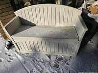 Front view of white outdoor plastic bench with storage under seat on snowy surface.