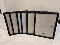 Six black 9.5x12 picture frames shown arranged leaning against wall.
