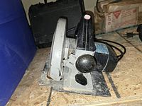 Side view of Rockwell skill saw showing blade guard, black handle, and base plate on a dusty surface.