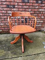 Front view of antique oak Captain's swivel chair showing curved arms, turned spindles, and solid base.