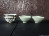 Six Asian bowls arranged in two groups: four with colorful dragon and phoenix designs stacked and two plain light green bowls on the right.