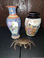 Front view of two Asian vases and bronze crab on black surface against wooden background