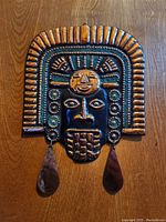 Frontal view of the copper and ground gemstone decorative mask showing full face and headgear with two hanging teardrop elements.