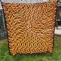 Front view of the crocheted afghan blanket with Rastafarian color spiral pattern and black border, displayed outdoors against a fence.