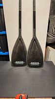 Two black iRocker paddle blade attachments standing upright against a white background, showing blade side with logo.
