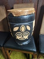 Front view of drum showing carved tribal mask design on black painted drum body with natural pelt top