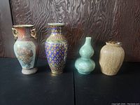 Front view of four vases arranged side by side against a dark wood background, showing size and decorative details.
