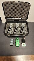 Three Pyle Pro microphones in a foam-padded carrying case with three guitar effect pedals (loop station, overdrive, tuner) placed below.