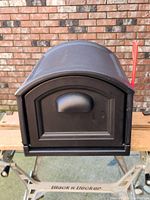 Front view of new black Step2 Town-to-Town XL mailbox with red flag, mounted temporarily on a work table.