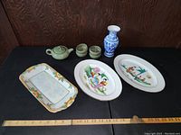Overview of the six items on a dark surface with wood background: three platters, small teapot and cups, and blue and white vase.