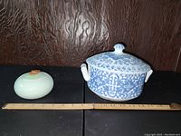 Blue and white rice bowl and small celadon dish side by side on black surface with wooden ruler showing measurement