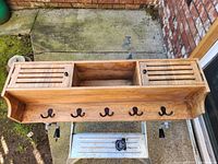 Top view of the wooden mounted storage unit showing two small cupboards with slatted doors, a central open shelf, and five metal coat hooks along the lower front.