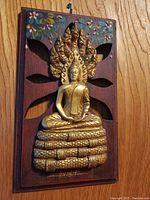 Front view of Thai Buddha wall art showing gold carved Buddha on serpent and floral painted wooden plaque