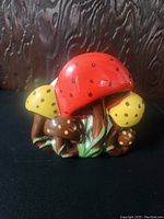 Front view of a vintage ceramic mushroom napkin holder showing the red and yellow spotted mushroom caps with grass details at the base.