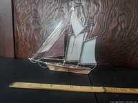 Photo of vintage stained glass sailboat from front angle with wooden ruler for size reference indicating approximately 9 inches wide.