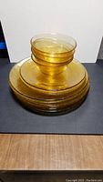 Stack of 6 amber/gold textured dinner plates with 4 small plates and 4 bowls stacked on top against a white background.