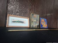 Three vintage wall art pieces displayed side by side: a framed hand painted feather with lizard, pressed flowers under glass, and a colorful owl tile trivet.